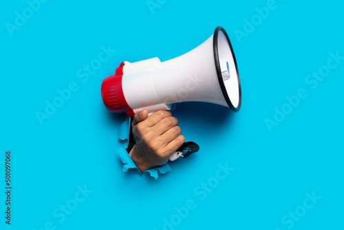 hand holds a megaphone blue background out of a torn hole in a paper background