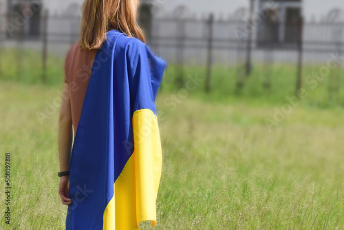 A young girl stands, covered with the national flag of Ukraine, against the backdrop of a local park. photo
