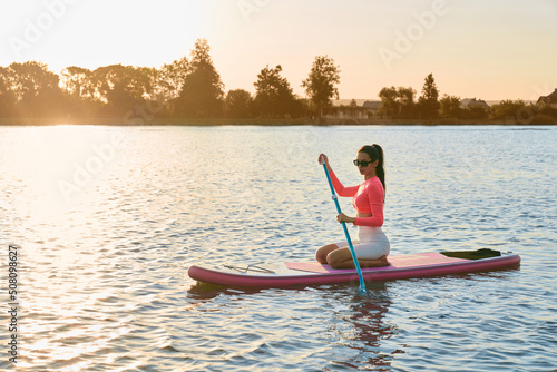 Caucasian sporty woman spending evening time on lake for practising in paddle boarding. Concept of people, active hobby and healthy lifestyles.