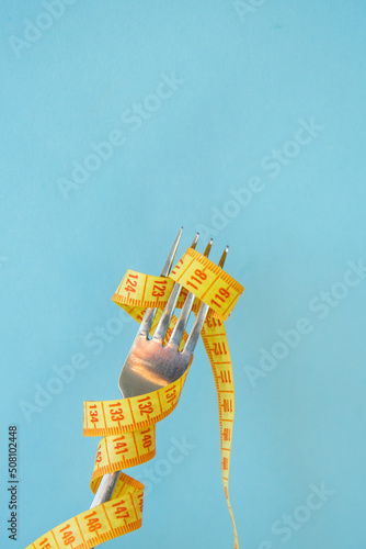 Bright yellow measuring tape on fork on a blue background. Diet concept