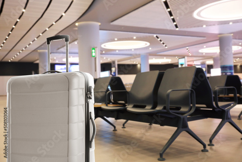 Stylish white suitcase in waiting area at airport terminal