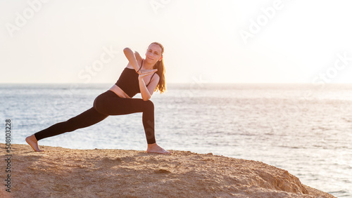 Young fitness woman doing twisting yoga pose at the beach in the morning. Yoga morning routine image
