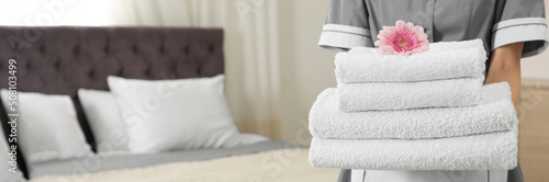 Fototapeta Chambermaid with stack of fresh towels in hotel room, closeup view with space for text