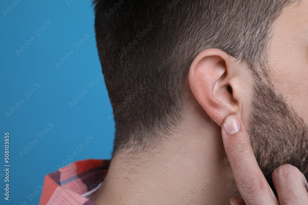 Naklejka premium Man pointing at his ear on light blue background, closeup