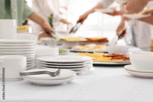 People taking food during breakfast, focus on clean dishware. Buffet service