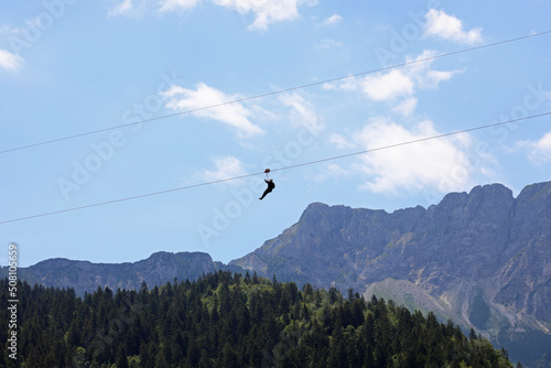 fearless person hanging from the steel cable that connects the opposite slopes of the mountain and the force of gravity that drags down