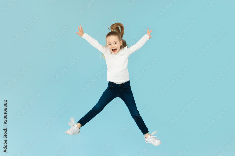 Obraz premium Joyful Little Girl Jumping Having Fun Posing, Blue Background