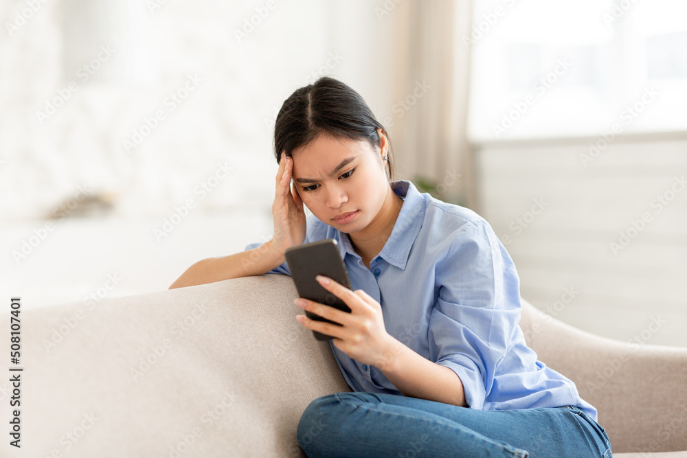 Concentrated asian woman sitting on couch, using cell phone Concentrated asian woman sitting on couch, using cell phone