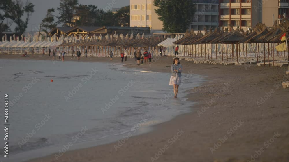 Single woman walking at seashore, waving splash at coastline, sunset panorama Single woman walking at seashore, waving splash at coastline, sunset panorama