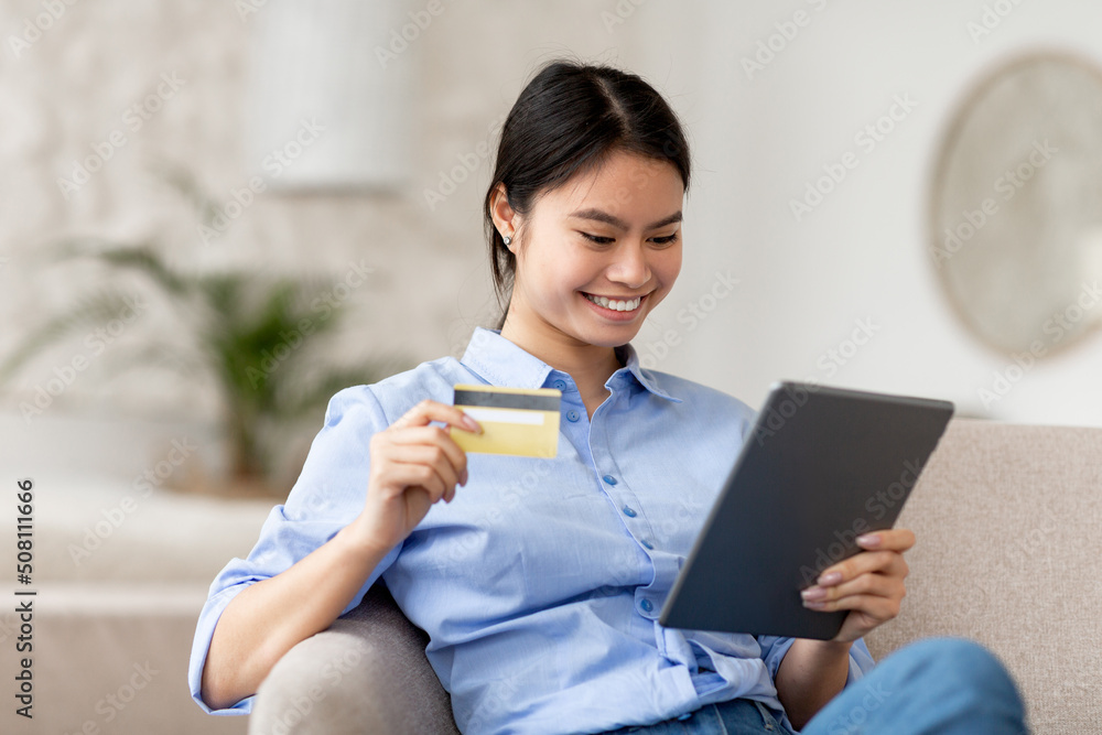 Cheerful japanese woman shopping online, using pad and credit card Cheerful japanese woman shopping online, using pad and credit card