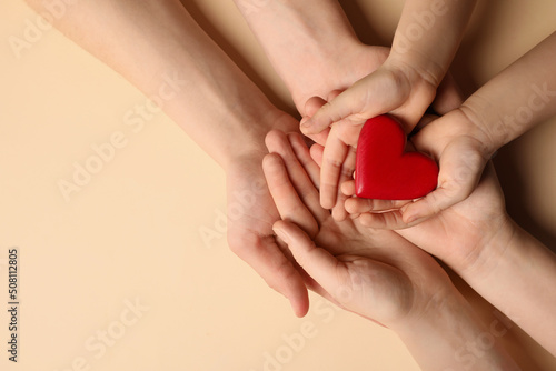 Parents and kid holding red heart in hands on beige background, top view