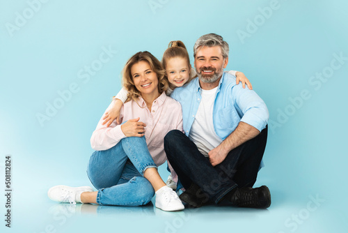 Cheerful Family Of Three Embracing Posing Together On Blue Background