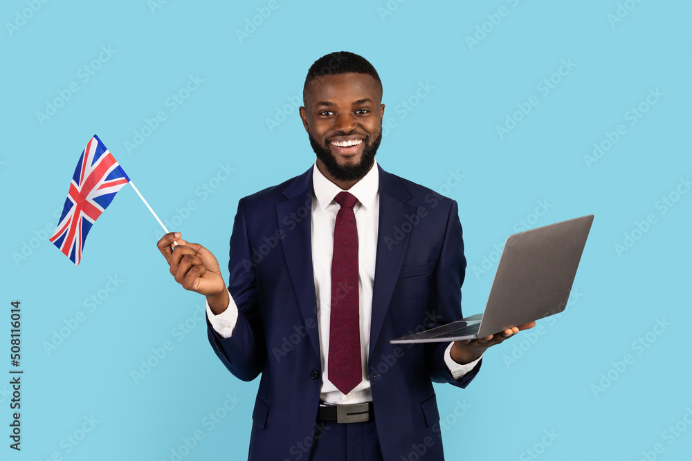 Handsome Black Businessman In Suit Holding Laptop And British Flag Handsome Black Businessman In Suit Holding Laptop And British Flag