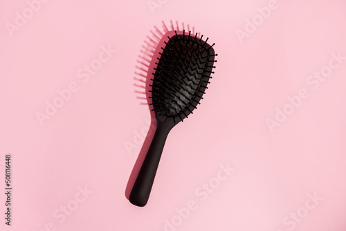 Black hair brush on pink background with copy space