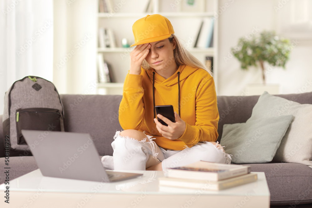 Disappointed young female looking at a mobile phone and sitting at home Disappointed young female looking at a mobile phone and sitting at home