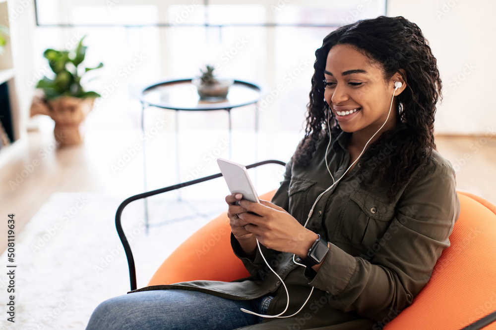 © Prostock-studio - Smiling black lady in headhones using cell phone © Prostock-studio - Smiling black lady in headhones using cell phone