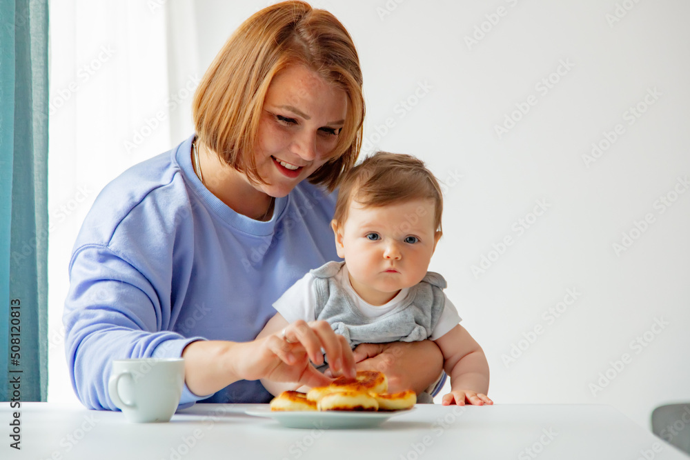 Ukrainian migrant mother with infant daughter sit at table with cheesecake on breakfast Ukrainian migrant mother with infant daughter sit at table with cheesecake on breakfast