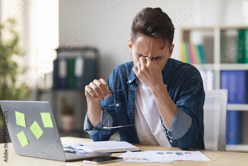 Deadline Stress. Overworked Male Entrepreneur Massaging Nosebridge At Workplace In Office photo