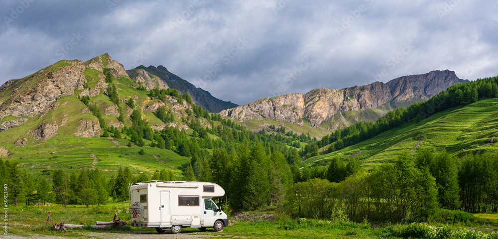 Camper van in the mountains, the Alps, Piedmont, Italy. Sunset dramatic sky and clouds, unique highlands and rocky mountains landscape, alternative vanlife vacation concept.