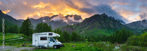 Camper van in the mountains, the Alps, Piedmont, Italy. Sunset dramatic sky and clouds, unique highlands and rocky mountains landscape, alternative vanlife vacation concept.