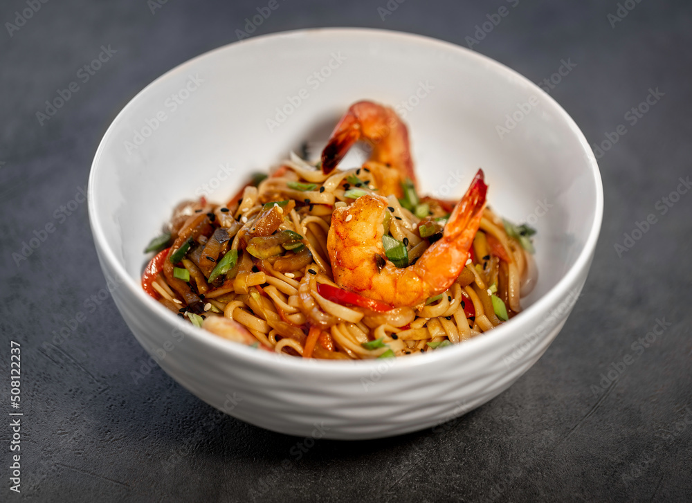 Asian udon noodles with shrimp, vegetables and teriyaki sauce on a black concrete background. Chinese and Japanese cuisine. Asian udon noodles with shrimp, vegetables and teriyaki sauce on a black concrete background. Chinese and Japanese cuisine.