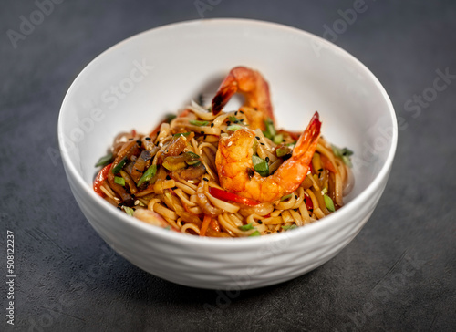 Asian udon noodles with shrimp, vegetables and teriyaki sauce on a black concrete background. Chinese and Japanese cuisine.