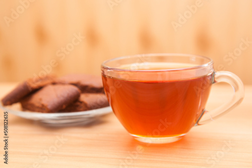 Cup of black tea on the wooden table and chocolate cookies on background