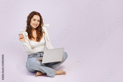 A woman sits with a laptop on a white background.