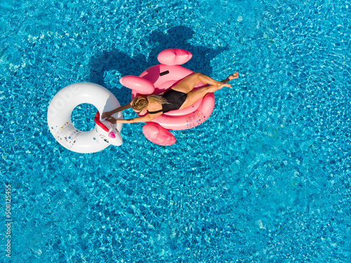 Woman on flamingo pool float and unicorn in pool. Summer holidays  enjoying summer vacations during quarantine.