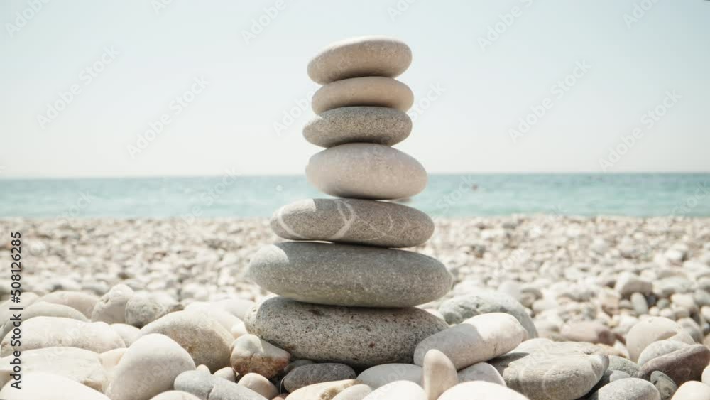 Close-up, a woman makes a cairn. Handmade stone tower on the seashore. A stack of balanced pebbles on the beach. Against the backdrop of the sea Close-up, a woman makes a cairn. Handmade stone tower on the seashore. A stack of balanced pebbles on the beach. Against the backdrop of the sea