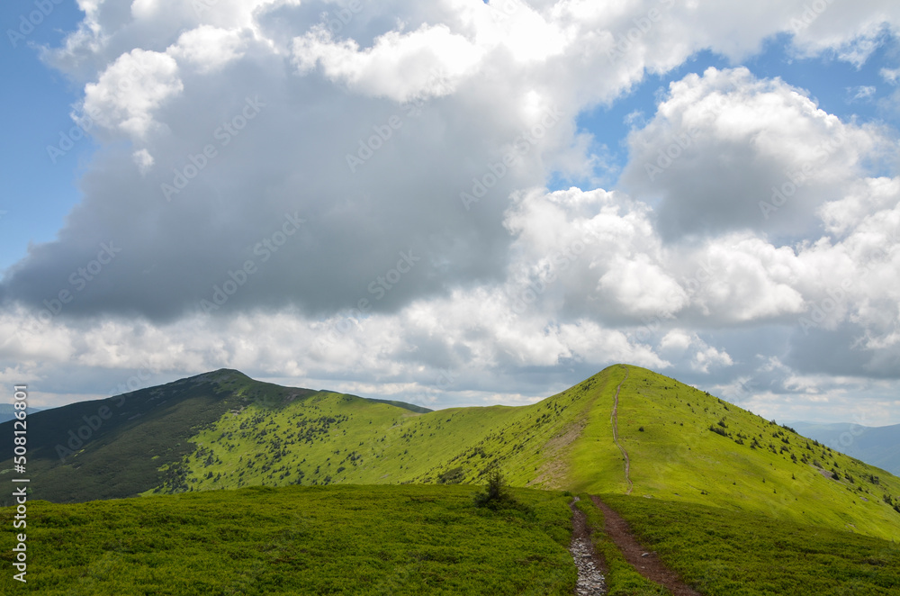 Beautiful ridge of mountains with lush green grass on tops and slopes on background of blue sky with clouds. Carpathians, Ukraine Beautiful ridge of mountains with lush green grass on tops and slopes on background of blue sky with clouds. Carpathians, Ukraine