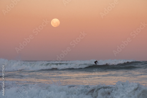 man surfing a wave under the full moon at sunset - Argentina
