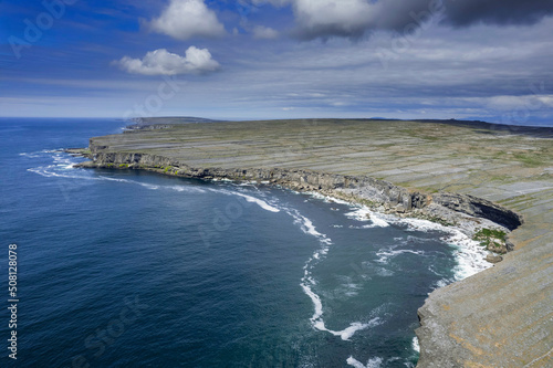 Ocean and cliffs and rugged stone terrain of Aran Island. Warm sunny day and blue cloudy sky. Popular travel tourism destination. Irish landscape.