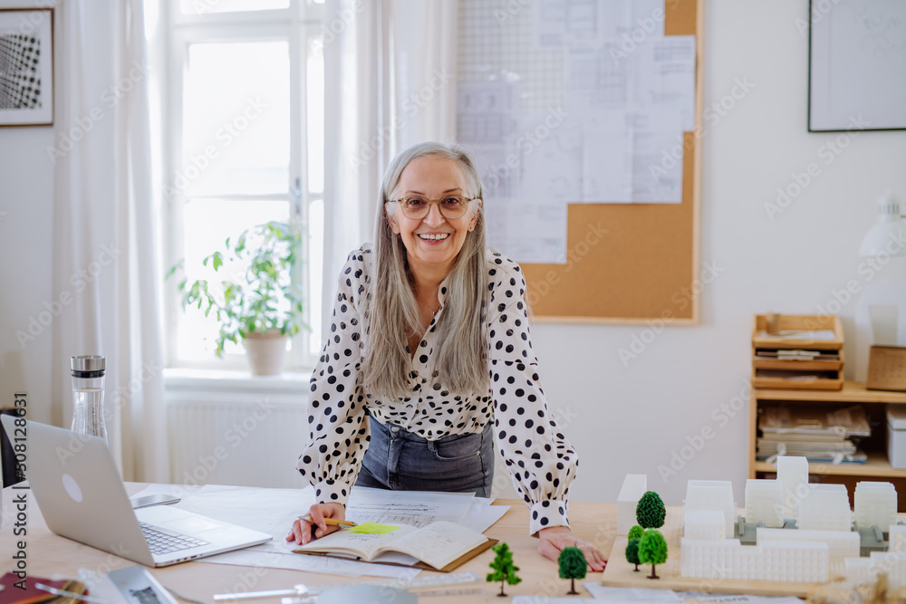 Mature woman architect with model of houses standing in office and looking at camera. Mature woman architect with model of houses standing in office and looking at camera.