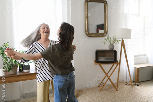Happy senior grandmother with teenage granddaguhter dancing together at home.