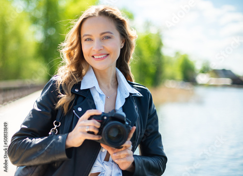 Fotografie Young smiling woman holding a reflex camera outdoor