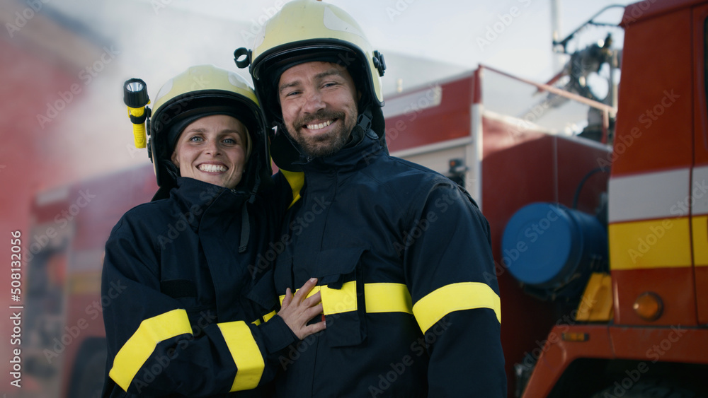Obraz premium Happy firefighters man and woman after action looking at camera with fire truck in background