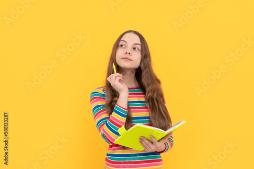 Thoughtful kid think over school essay holding pen and copybook yellow background, story photo