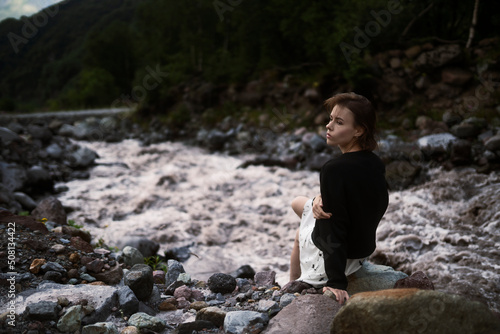 Young lovely girl is sitting on the stone and looking away.