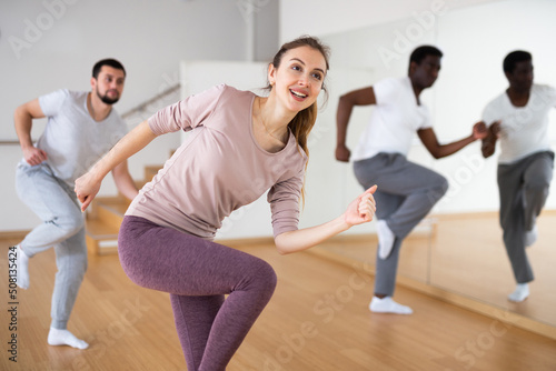 Portrait of cheerful young woman enjoying active dancing during group training in dance studio..