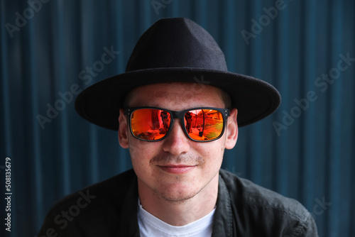 Smiling fashion man. Portrait of handsome smiling stylish hipster lambersexual model. Man dressed in red polarization sunglasses. Fashion male on the modern blue background. Face. Closeup. Portrait