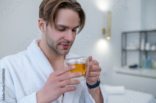 Young man in a white robe holding a cup of tea