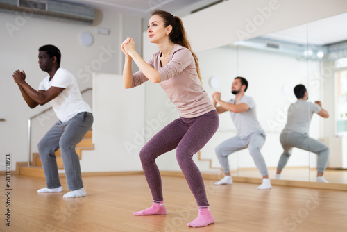 Group of people squatting during fitness training in studio.