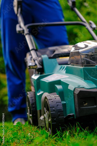 lawn mower close-up mows the lawn in the summer garden.Technique and equipment for the garden. Summer work in the garden. A man cuts green juicy grass with a lawn mower in a garden