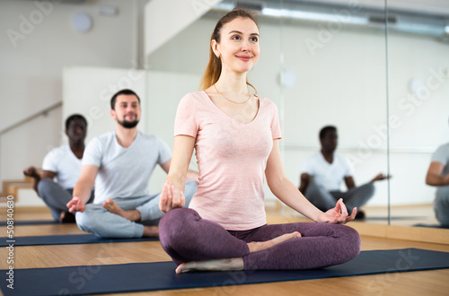 Young sporty woman enjoying meditation in modern yoga studio, sitting in lotus position while her hands resting on knees with fingers folded in mudra