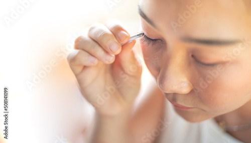 Female hand holding the eyelash and preparing to attach to her eye.