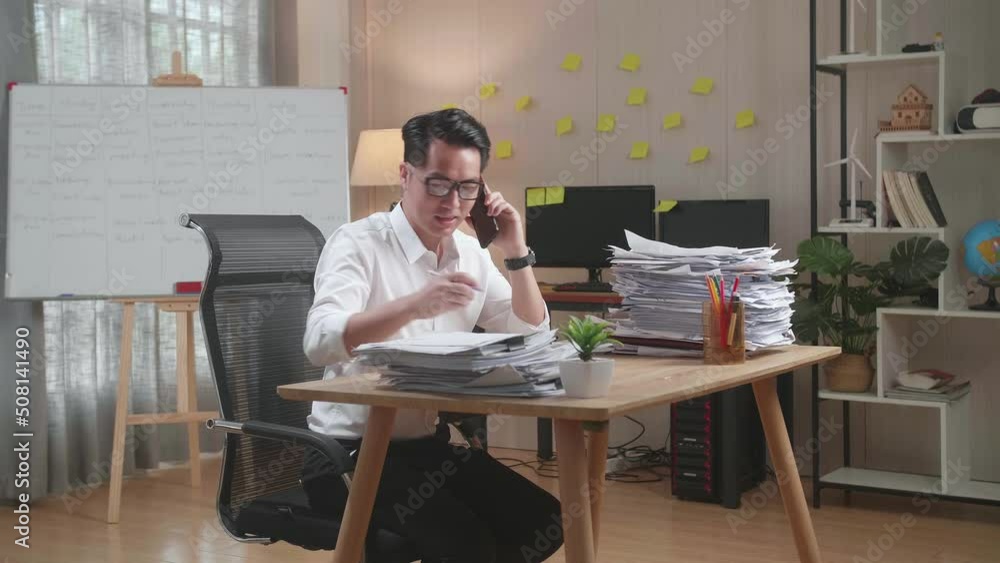 Asian Man Talking On Phone And Taking Note While Working Hard With Documents At Office
Asian Man Talking On Phone And Taking Note While Working Hard With Documents At Office