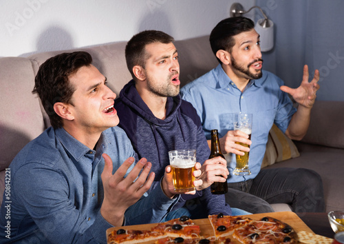 Group of happy cheerful positive male friends watching football match on tv at home and having fun together