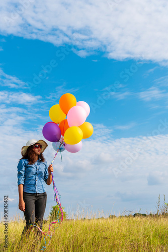 Woman holding balloons running on green meadow white cloud and blue sky with happiness Cheerful and relax. Hands holding vibrant air balloons play on birthday party happy times summer sunlight outdoor