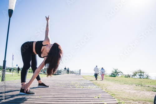 side view standing woman stretching muscles outdoors touching one foot with one hand, copy space